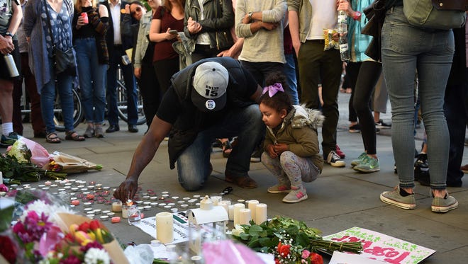 People watch as a man and a child light a candle alongside floral tributes in Albert Square in Manchester, northwest England on May 23, 2017, following a vigil in solidarity with those killed and injured in the May 22 terror attack at the Ariana Grande concert at the Manchester Arena.
