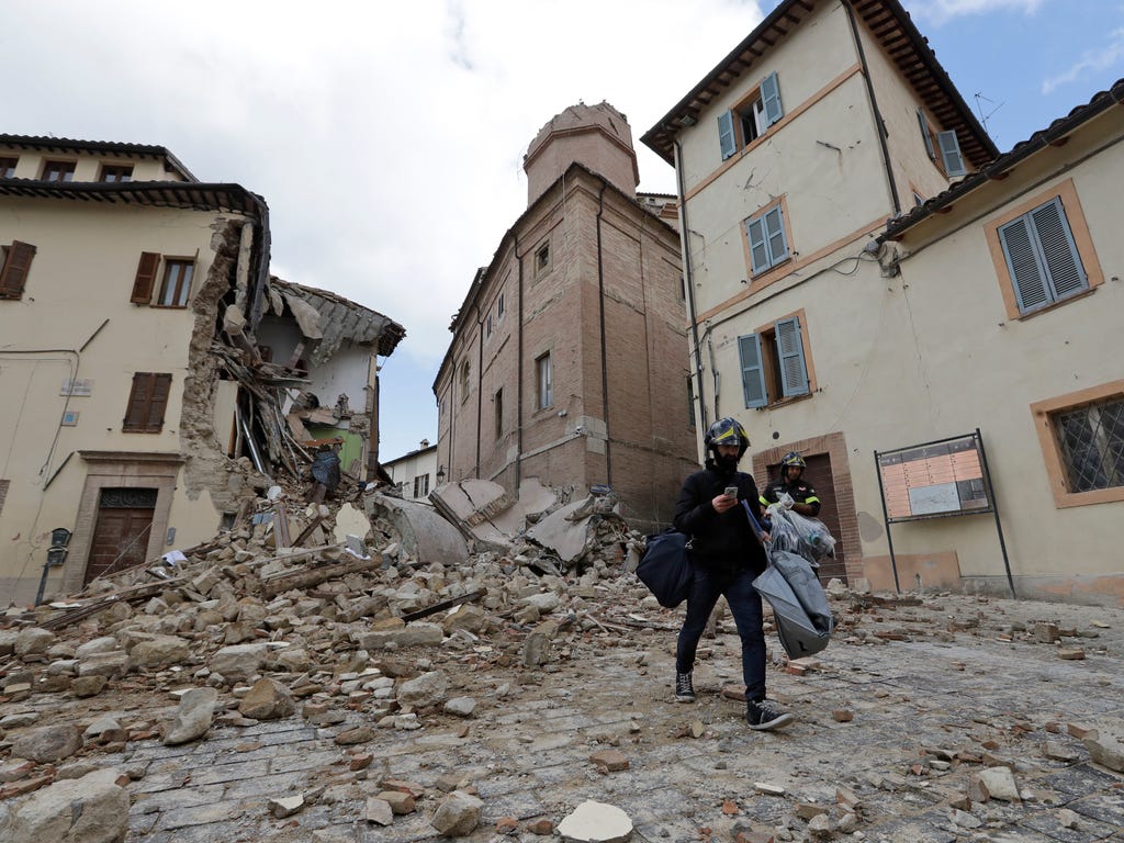 A resident carrying his belongings passes in front of the collapsed bell tower of the Santa Maria in Via church in the town of Camerino, in central Italy on Oct. 27, 2016, after a magnitude-5.9 earthquake destroyed part of the town. Authorities began