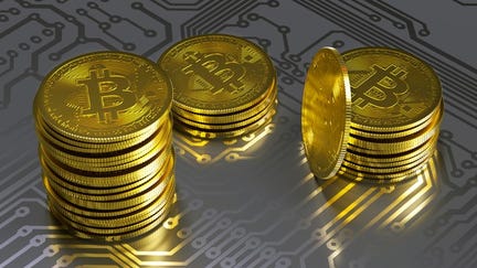 Stacks of physical gold bitcoin lying atop a gray...