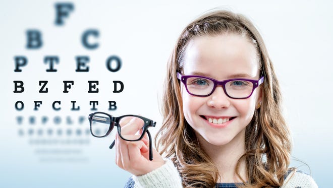 Girl holding glasses with test chart in background.