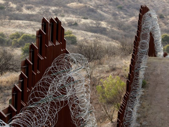 A border wall covered with razor wire separates the United States