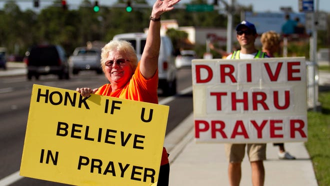 Lois Strauss waves to passers-by on South Tamiami Trail . Strauss and other church members hold signs to let drivers know they can pull in and pray.