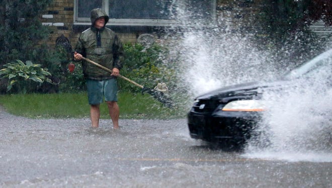 A  man tries to keep storm sewers open in front of his home at 60th and Clarke streets in Milwaukee as cars splash through flooded intersections as the result of heavy downpours. The weather made travel difficult as scattered thunderstorms moved through southeast Wisconsin  Monday, June 18, 2018, ahead of cooler weather.