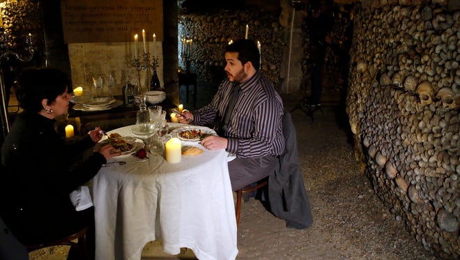 Guests Brazilian Pedro Arruda, 27, right, and his mother Monica, attend their dinner prior to spend the Halloween night in Paris' creepy Catacombs amid skulls and bones, in Paris, France, Saturday, Oct, 31, 2015. House-sharing company Airbnb has struck a spooky one-off deal with Paris' City Hall to sublet the subterranean ossuaries, the final resting place of 6 million bodies, on Nov. 31 to the winner of a worldwide competition. (AP Photo/Francois Mori)