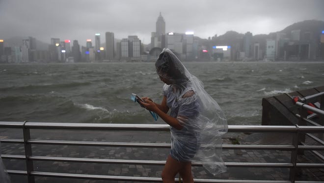 A woman uses her phone while wearing a plastic poncho along Victoria Harbour during heavy winds and rain brought on by Typhoon Hato in Hong Kong on Aug. 23, 2017. Typhoon Hato smashed into Hong Kong on Aug. 23 with hurricane force winds and heavy rains in the worst storm the city has seen for five years, shutting down the stock market and forcing the cancellation of hundreds of flights.