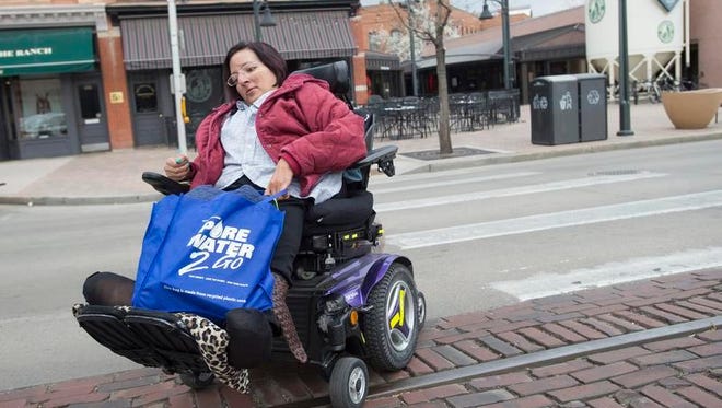 Vivian Armendariz steers her electric wheelchair around vehicles parked on Matthews Street as she runs errands in Old Town on Tuesday. Armendariz said she sometimes feels safer traveling in the street instead of uneven sidewalks.