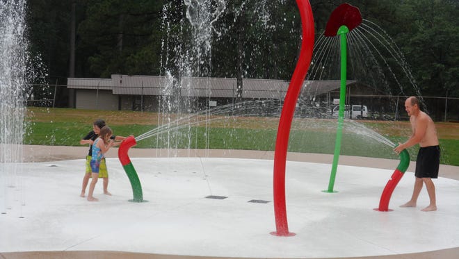 Dustin Schneider has a spray battle with his children, Evan, 8, and Camille, 5, on Friday morning at the city of Pineville's new splash pad at Kees Park. They were the first ones to try out the splash pad after it officially opened.