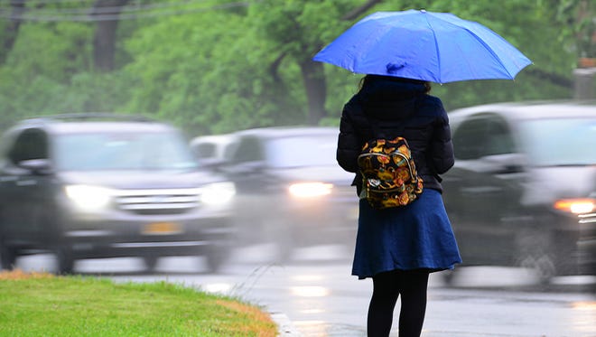 A woman uses an umbrella to shield herself from the rain as she waits for her ride along Route 4 westbound in Teaneck on Thursday May 17, 2018. 