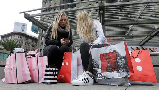 FILE - In this Nov. 25, 2016, file photo, Maddy, left, and her friend Maggie, sit with their shopping bags at Union Square in San Francisco. The holiday shopping season is losing some of its power in the year's sales. November and December now account for less than 21 percent of annual retail sales at physical stores, down from a peak of over 25 percent. The shift is in part because people are spreading out their shopping all year, demanding big discounts and spending more on events rather than more stuff.