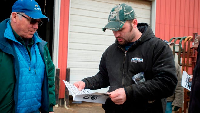In this Friday, April 6, 2018 photo, Nate Elzinga, right, looks over the auction brochure during the dairy cow auction at his farm in Zeeland, Mich. Friday was the day of the auction where Elzinga and his partners sold the herd. Market forces and larger milking operations made it difficult for them to be profitable.