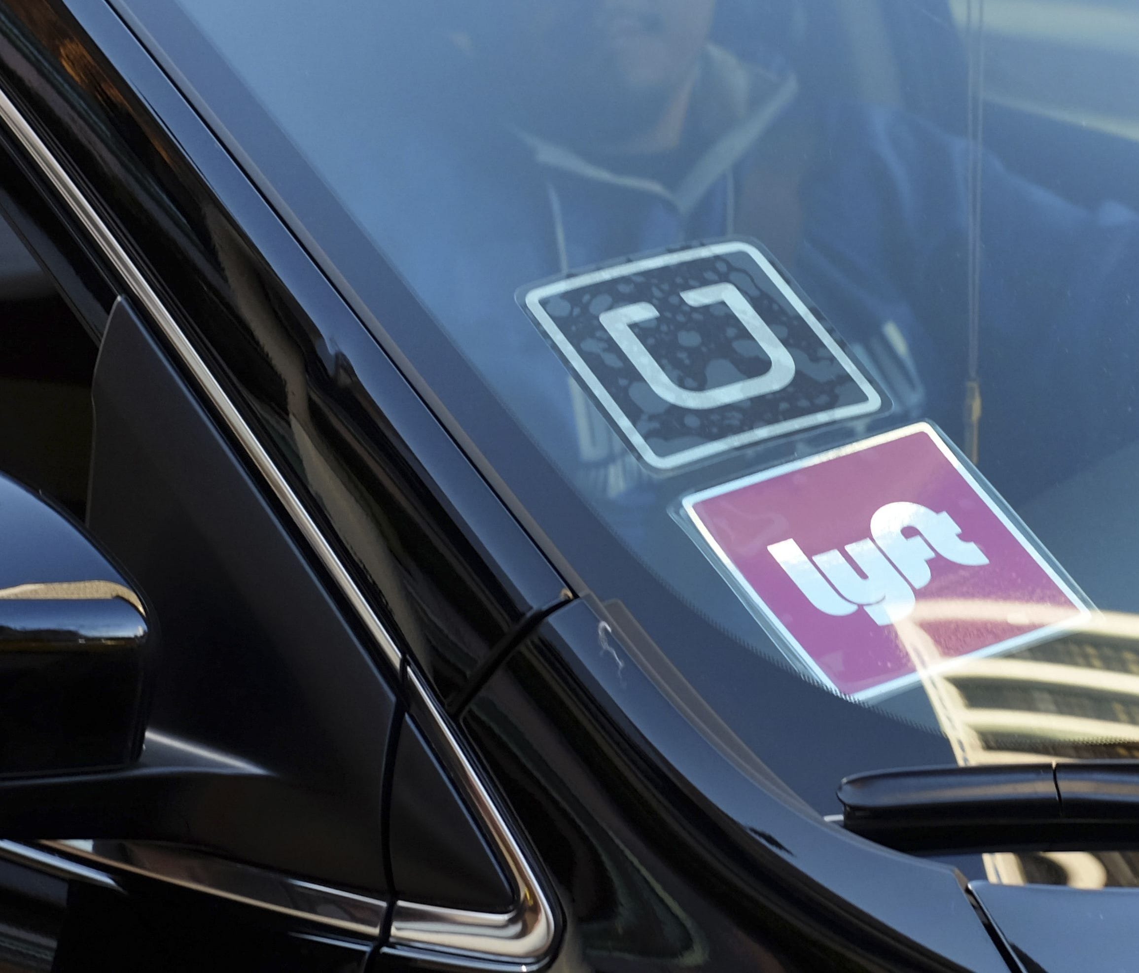A driver displaying Lyft and Uber stickers on his front windshield drops off a customer.