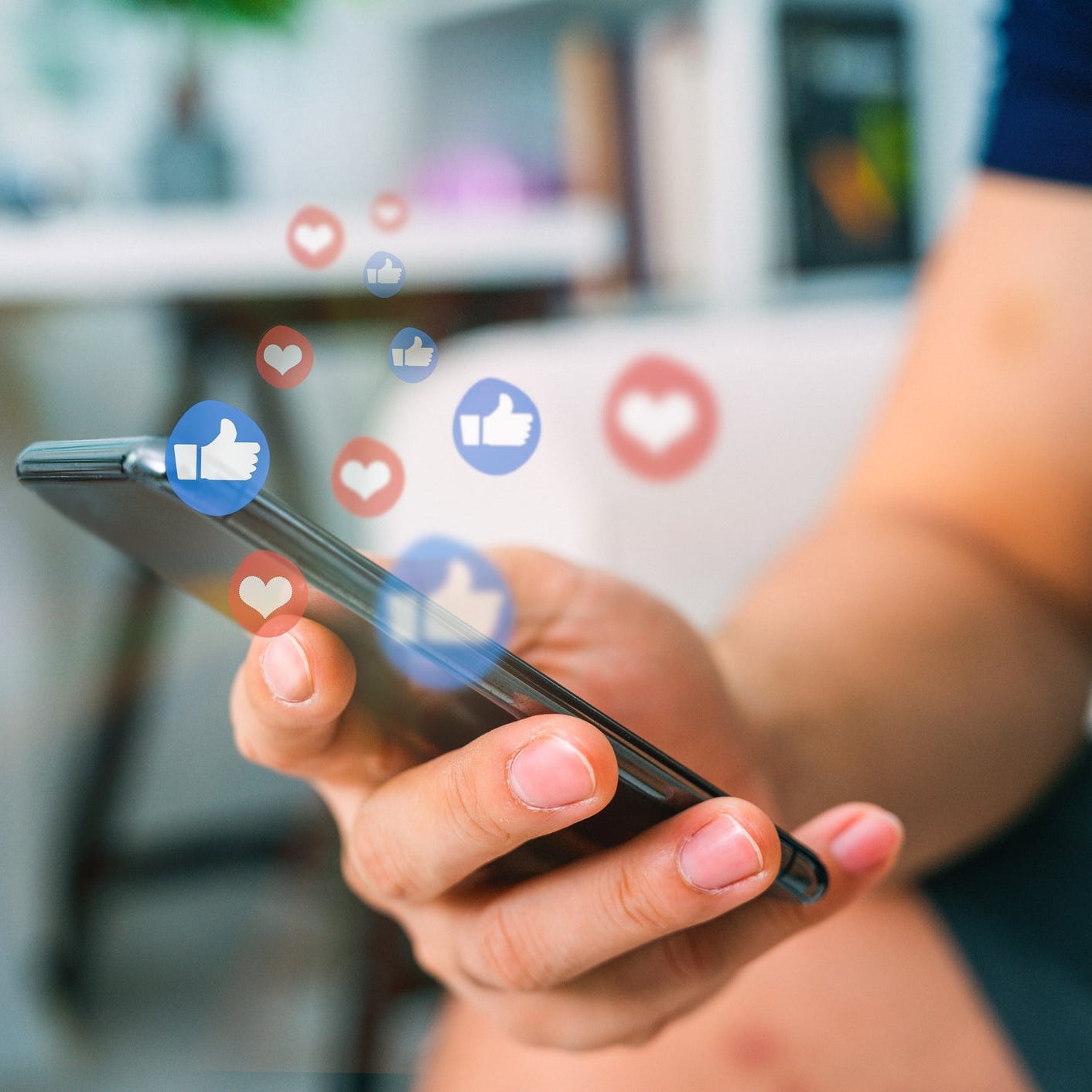 Someone works a smartphone as heart and thumbs-up emojis emanate into the air around it.