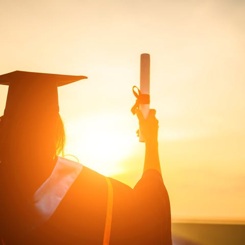 A college graduate in cap and gown holding up a di