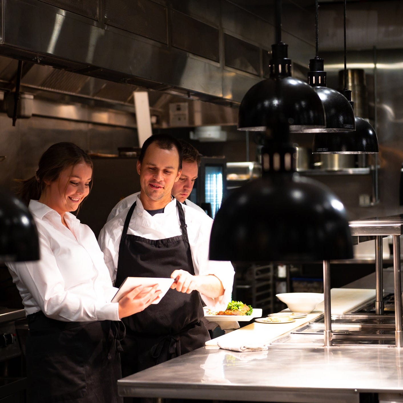 Three restaurant workers looking at a tablet.
