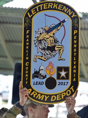 Spec. Tiffany Koziar hoists a cardboard cutout of the new anniversary coin. Letterkenny Army Depot is hosting a ceremony commemorating the depot’s 75th year of providing support to the DOD. Anniversary coins were sponsored by Patriot Federal Credit Union. The artwork was created by Depot employee Danny Kissel.