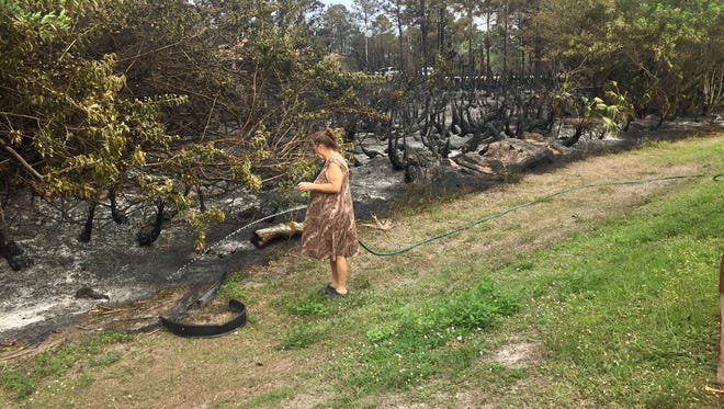 Roslyn York waters the line where the fire stopped next to her house Friday night in Lehigh Acres.