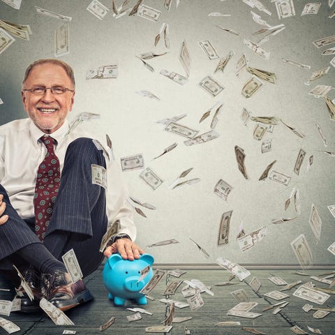 Man sitting and smiling with money falling all aro