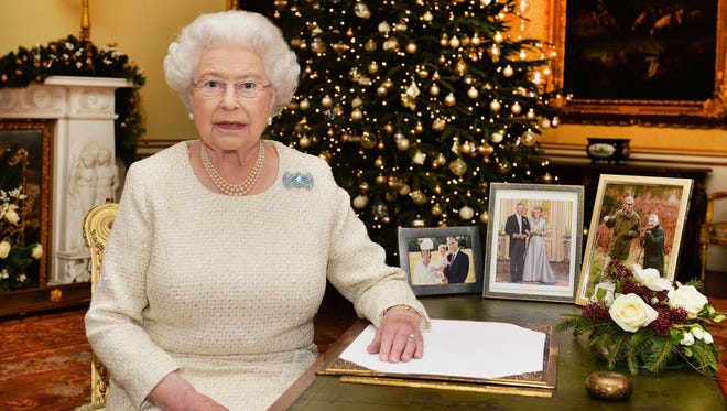 Britain's Queen Elizabeth II sits at a desk in the 18th Century Room in Buckingham Palace in London, after recording her Christmas Day broadcast to the Commonwealth, to be broadcast Friday, Dec. 25, 2015.  Pictures on the desk are members of the Royal family, from right, Queen Elizabeth with Duke of Edinburgh,  Prince Charles with Camilla Duchess of Cornwall, and Prince William with Kate and their children Prince George and Princess Charlotte.