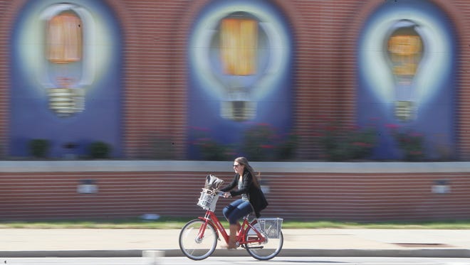 A bicyclist zips past a Duke Energy substation at Central Parkway and Plum Street that features paintings of six antique light bulbs.