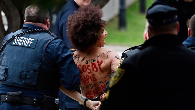 A topless protester was  detained after trying to ambush Bill Cosby as he arrived for the first day of his sexual-assault retrial.