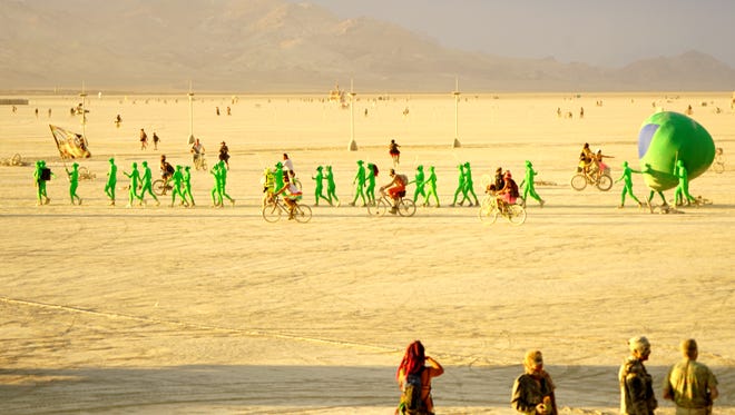 A line of little green men walk into the bright sunlight of the setting sun at Burning Man on Tuesday evening.