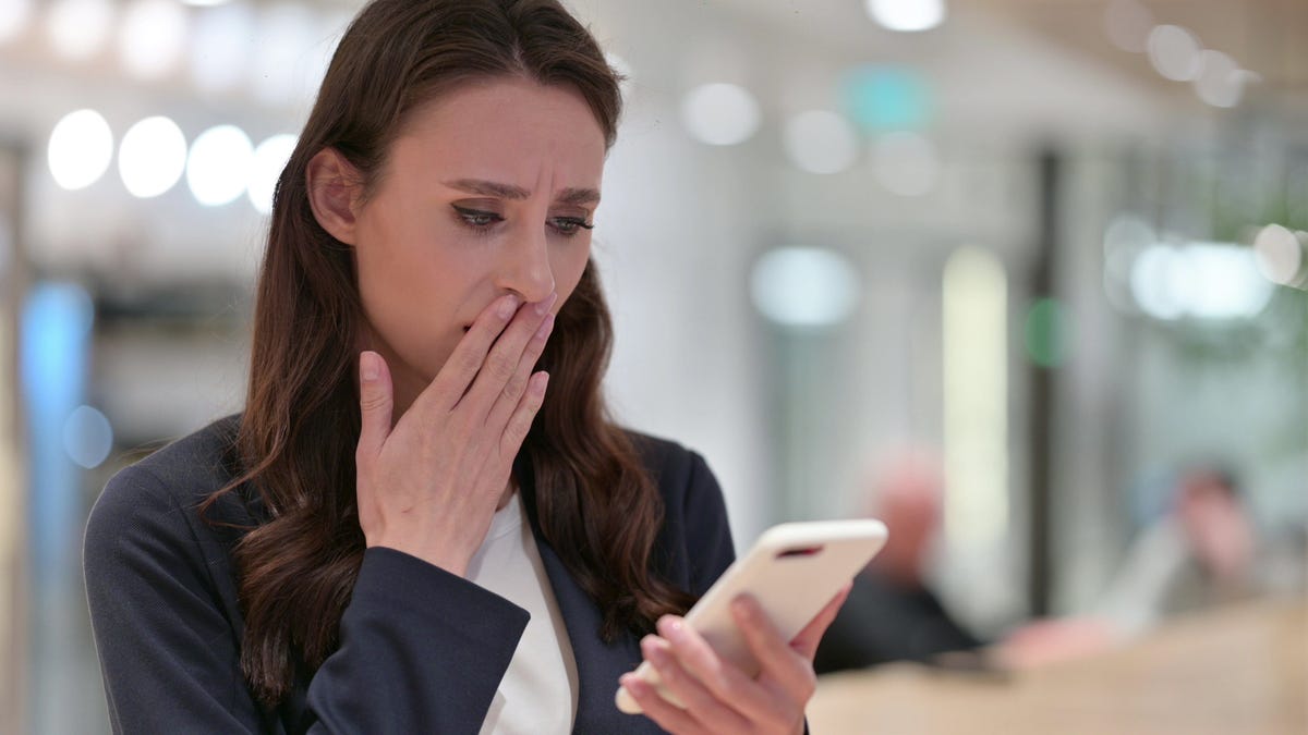 A concerned woman looks at her smartphone.