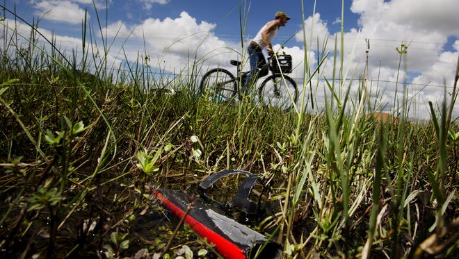 Cape Coral resident Adam Hitchins commutes to his job along Diplomat Parkway near the intersection of Andalusia Boulevard on Monday.  In the foreground is a piece of down tube from a bicycle with a water bottle attached.  Cyclist Scott Johnsen was killed by a car driven by Jason William Stewart Sunday at this location.  Found nearby was a bicycle speedometer/odometer and a clif bar.