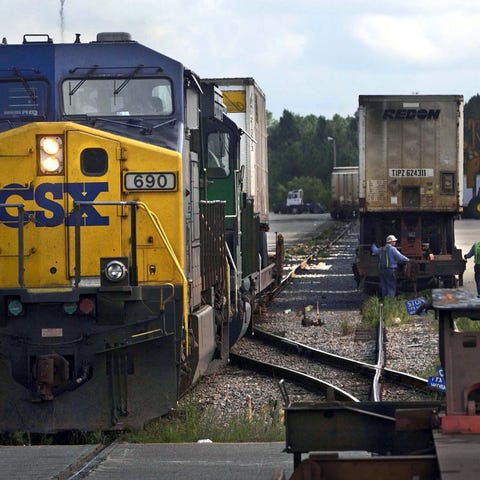 Workers repair a rail car as a train comes into th