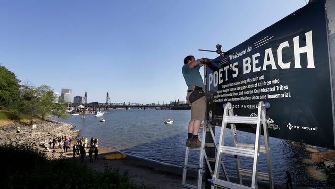 In this Thursday, July 6, 2017 photo, Curt Ellsworth puts up a sign at a section of newly formed beach, named Poet's Beach, on the Willamette River in downtown Portland, Ore.