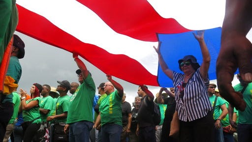 People carry a large Puerto Rican flag as they protest looming austerity measures amid an economic crisis and demand an audit on the island's debt to identify those responsible, in San Juan, Puerto Rico, Monday, May 1, 2017. Puerto Rico is preparing to cut public employee benefits, increase tax revenue, hike water rates and privatize government operations, among other things.