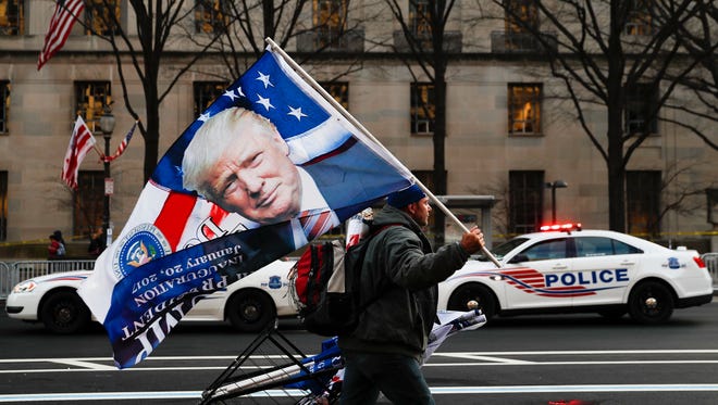 A street vendor holds a flag bearing the likeness of President-elect Donald Trump as he passes a line of police vehicles on Pennsylvania Avenue in Washington, Thursday, Jan. 19, 2017, ahead of Friday's presidential inauguration. (AP Photo/John Minchillo)