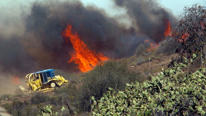 In this May 2, 2013, file photo, a bulldozer helps clear a hill near a fire in Thousand Oaks. Not all firefighters carry a hose or a shovel.