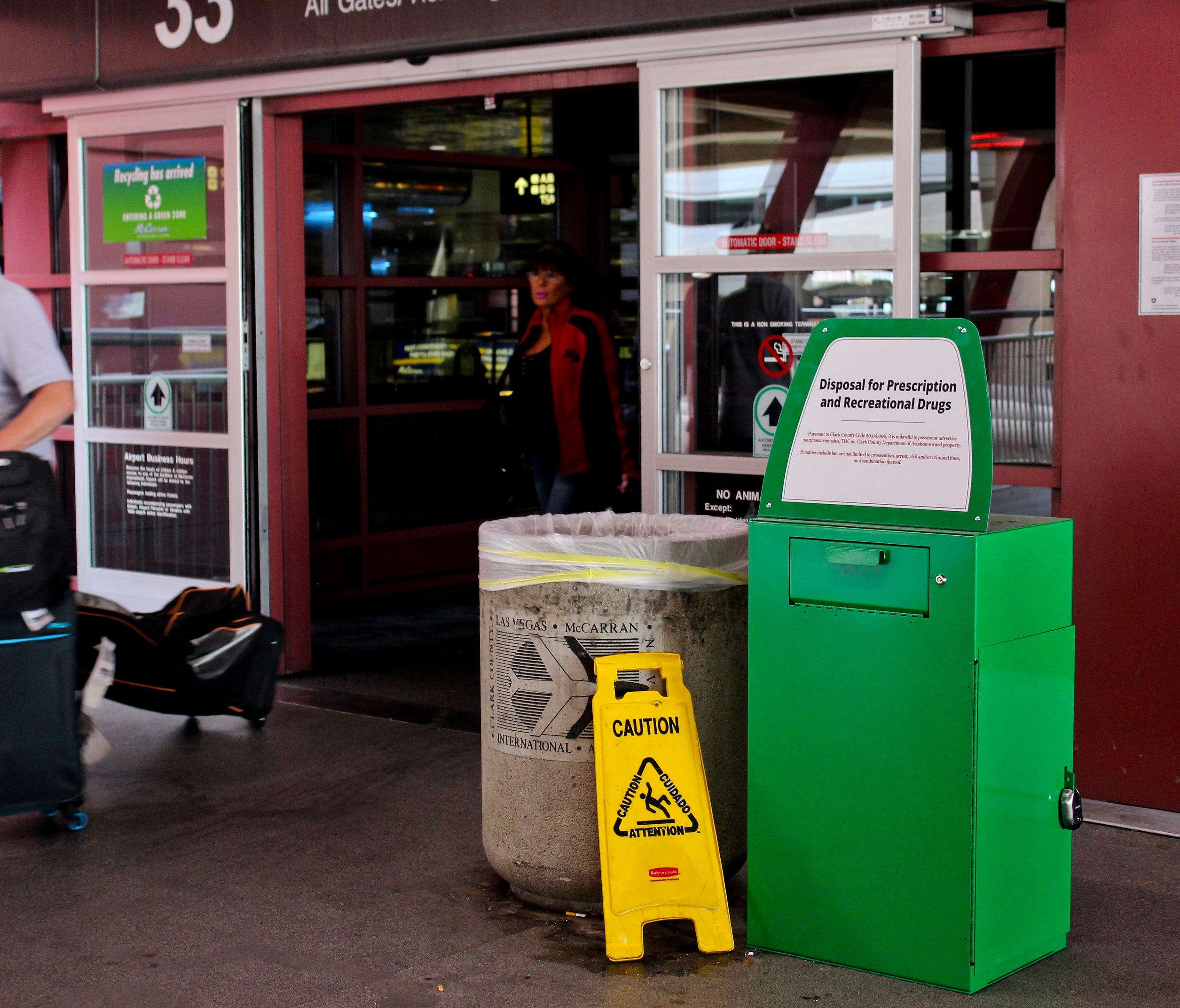 Unidentified travelers exit the airport past a green metal container designed for 