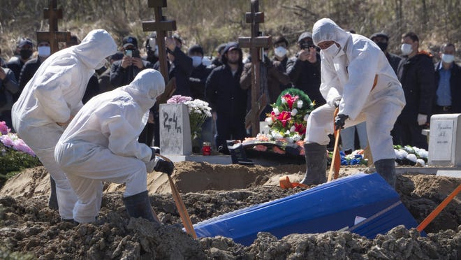 Grave diggers wearing protective suits bury a COVID-19 victim as relatives and friends stand at a safe distance, in the special purpose for coronavirus victims section of a cemetery in Kolpino, outside St.Petersburg, Russia, Sunday, May 10, 2020.