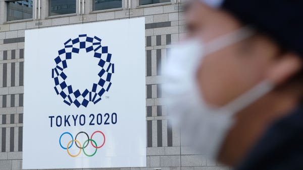 A man wearing a mask passes the logo of the Tokyo 