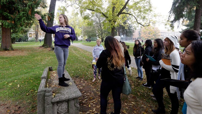 In this photo taken Tuesday, Oct. 15, 2013, University of Washington sophomore Megan Herndon, of Kailua, Hawaii, stands on a bench as she leads high school students on a tour of the campus in Seattle.