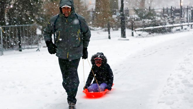 A man pulls his child through the snow while walking through Washington Square Park in New York.