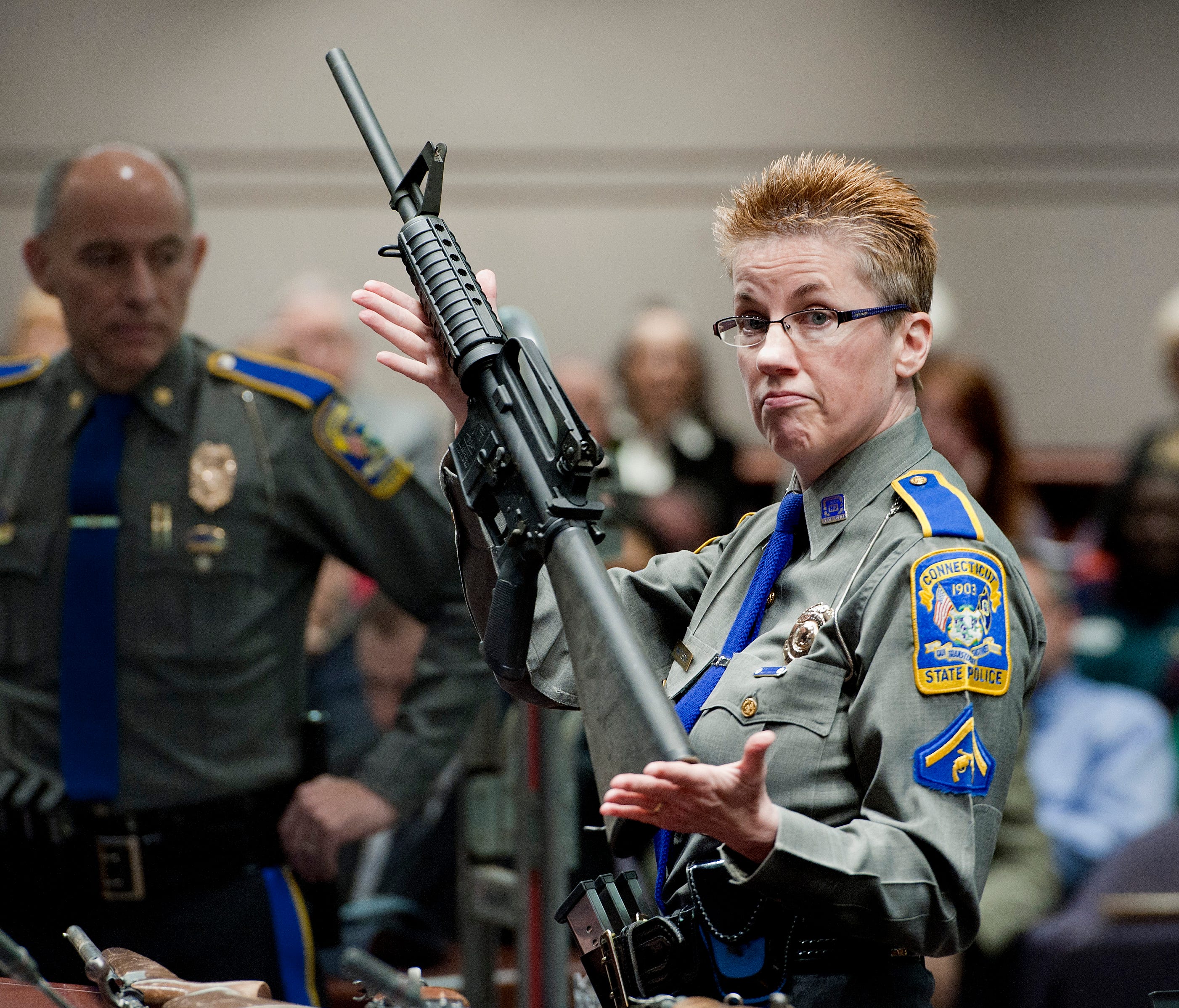 Firearms training unit Detective Barbara J. Mattson, of the Connecticut State Police, holds up a Bushmaster AR-15 rifle, the same make and model of gun used by Adam Lanza in the Sandy Hook School shooting, during a hearing of a legislative subcommitt