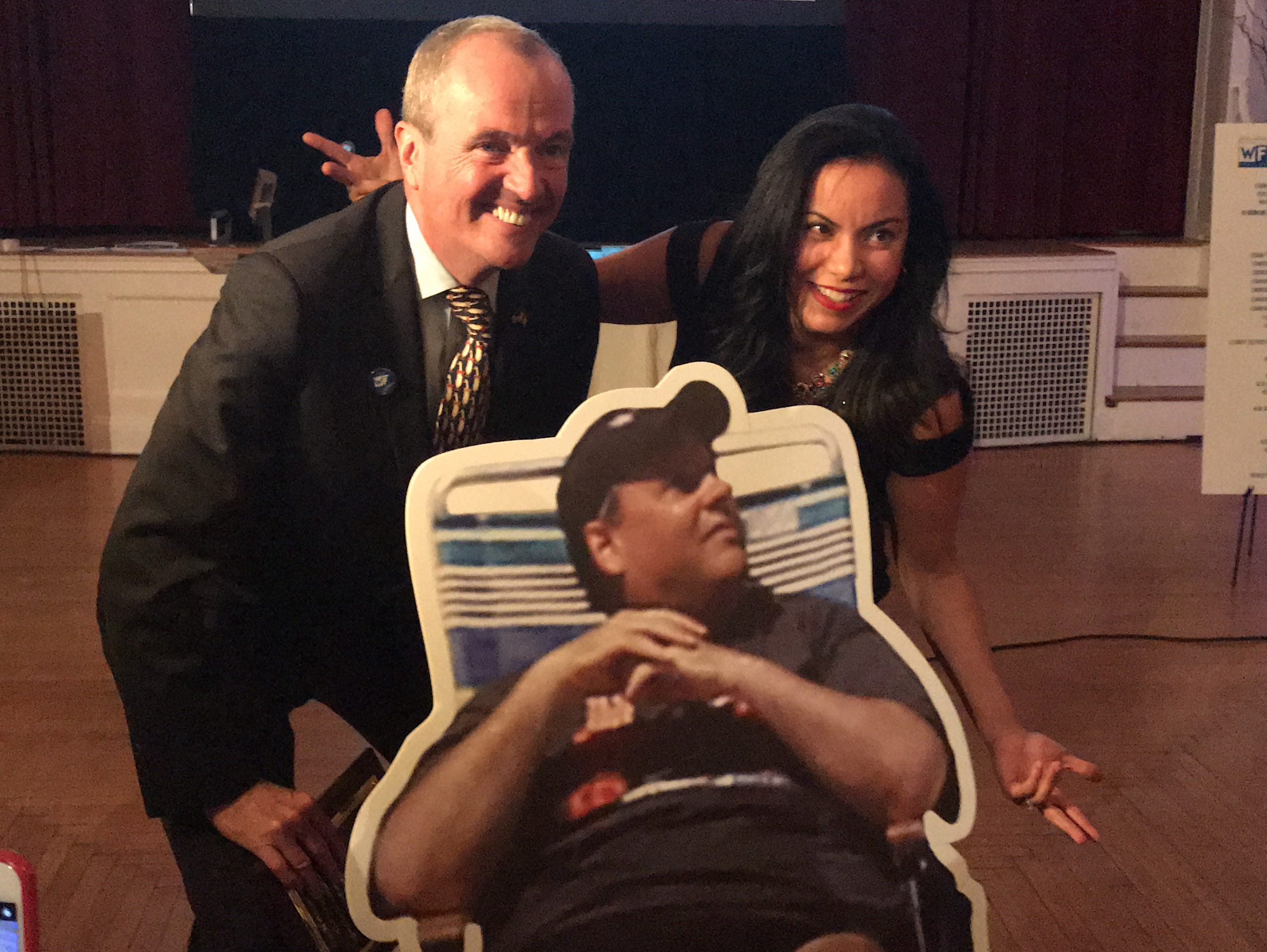 Governor-elect Phil Murphy stands behind cutout of Chris Christie in beach chair with Analilia Mejia of the New Jersey Working Families Alliance.