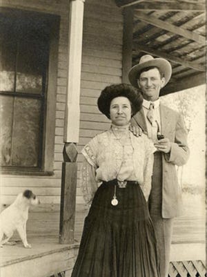 An unidentified Tempe couple poses with their dog for a 1910 postcard in front of a frame house with a broad wrap-around porch used for sleeping in the summer.