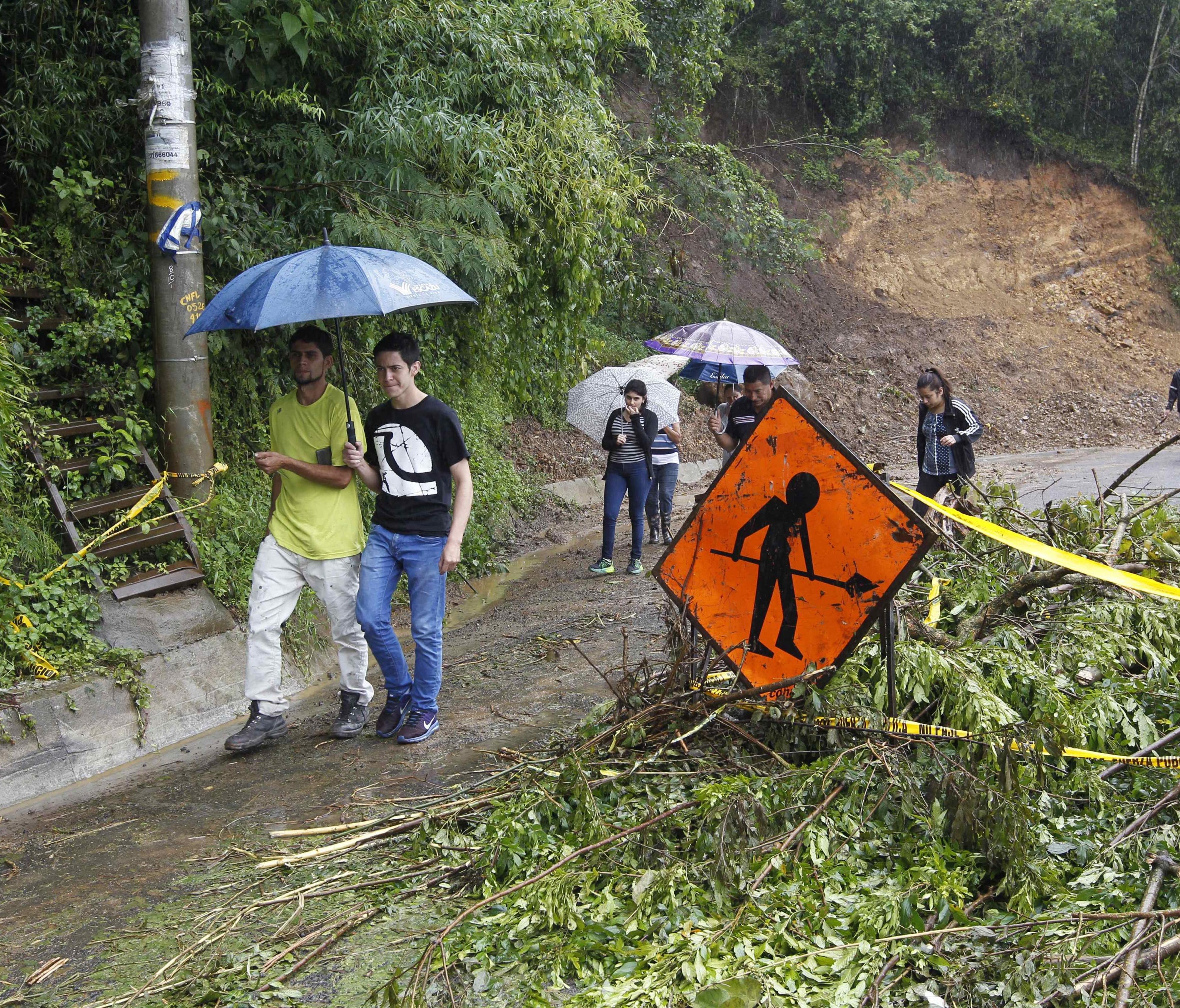 People walk pass by a debris filled road at the Llano area in Alajuelita, south San Jose, Costa Rica, Oct. 5, 2017.