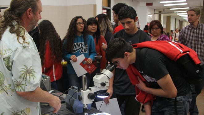 Richie Chacon peers into a microscope presented at a booth during the Loving High School college and career readiness fair.