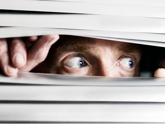 Fearful man looking sideways through venetian blind