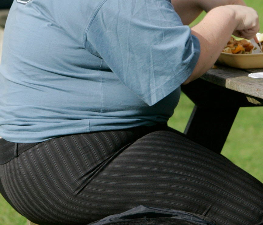 Overweight person eats at a bench.