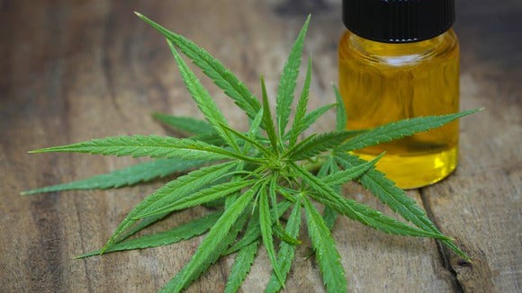 A bottle of cannabis oil next to a cannabis leaf.