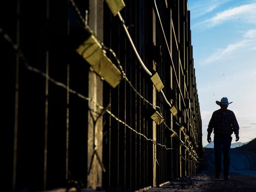 Rancher John Ladd walks along the border fence on his