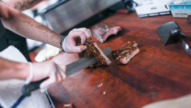 Carvers cut ribs and other barbecued meats at the counter as customers watch at Slows Bar BQ's new SlowsGR location in Grand Rapids' Downtown Market.