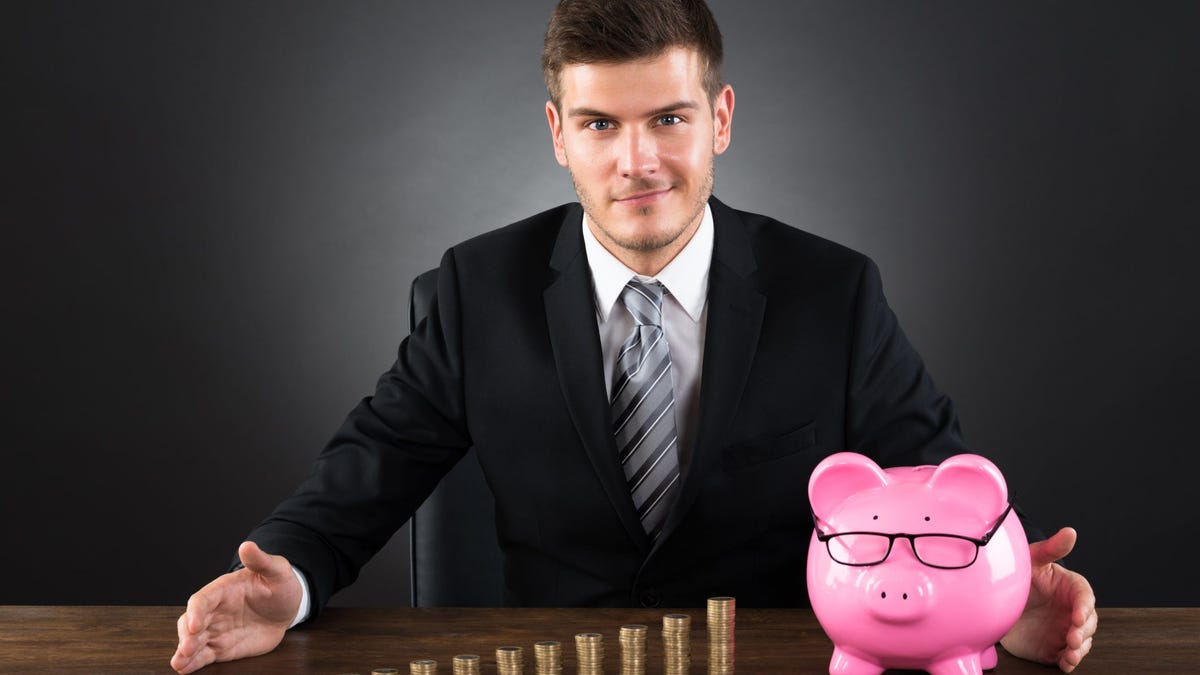Smiling man sitting in front of piggy bank with coins stacked next to it.