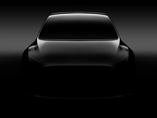A "teaser" photo of a silver Tesla Model Y, a sleek SUV, viewed from the front.