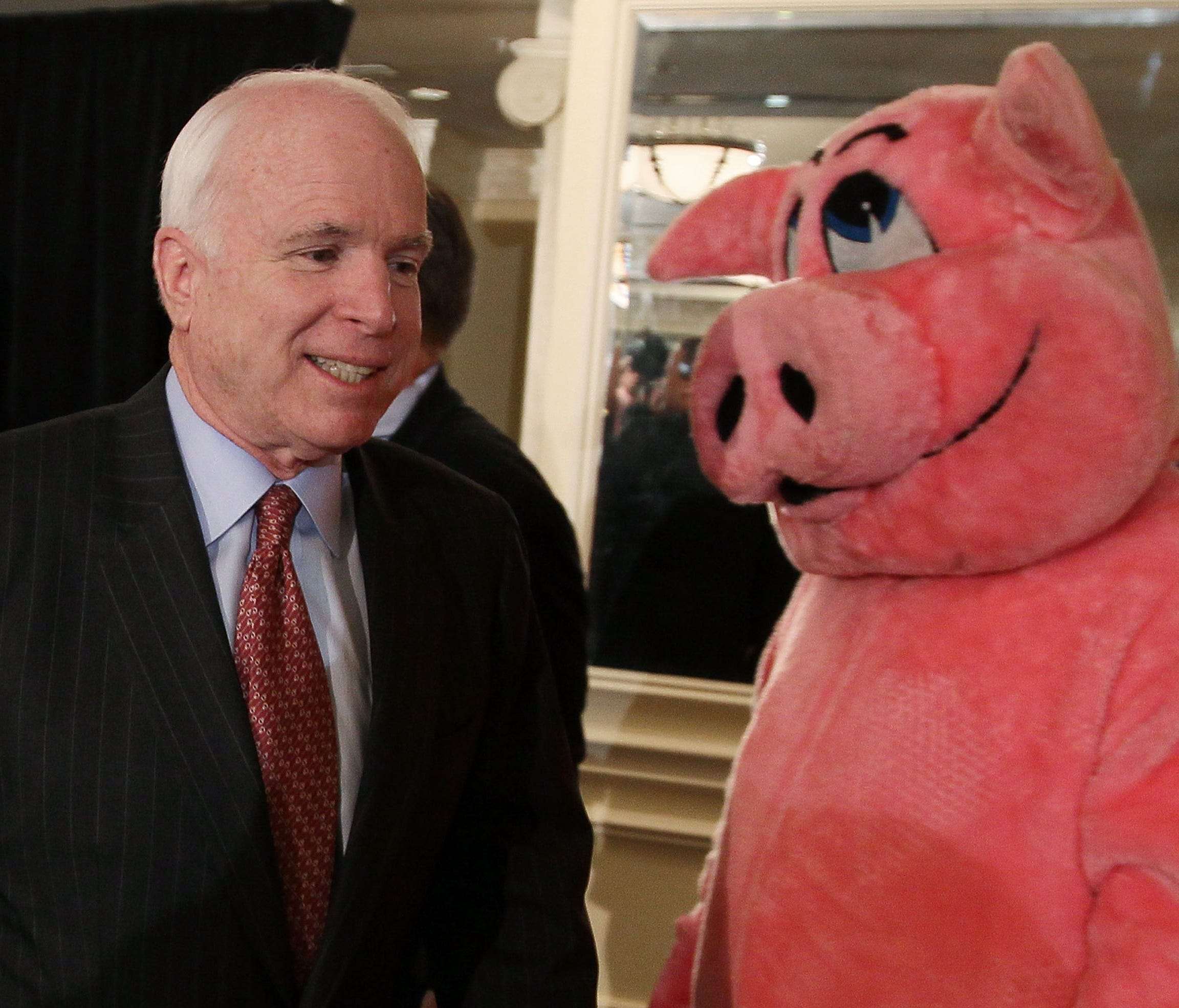 John McCain walks by a person in a pig costume on April 14, 2010 in Washington, D.C.